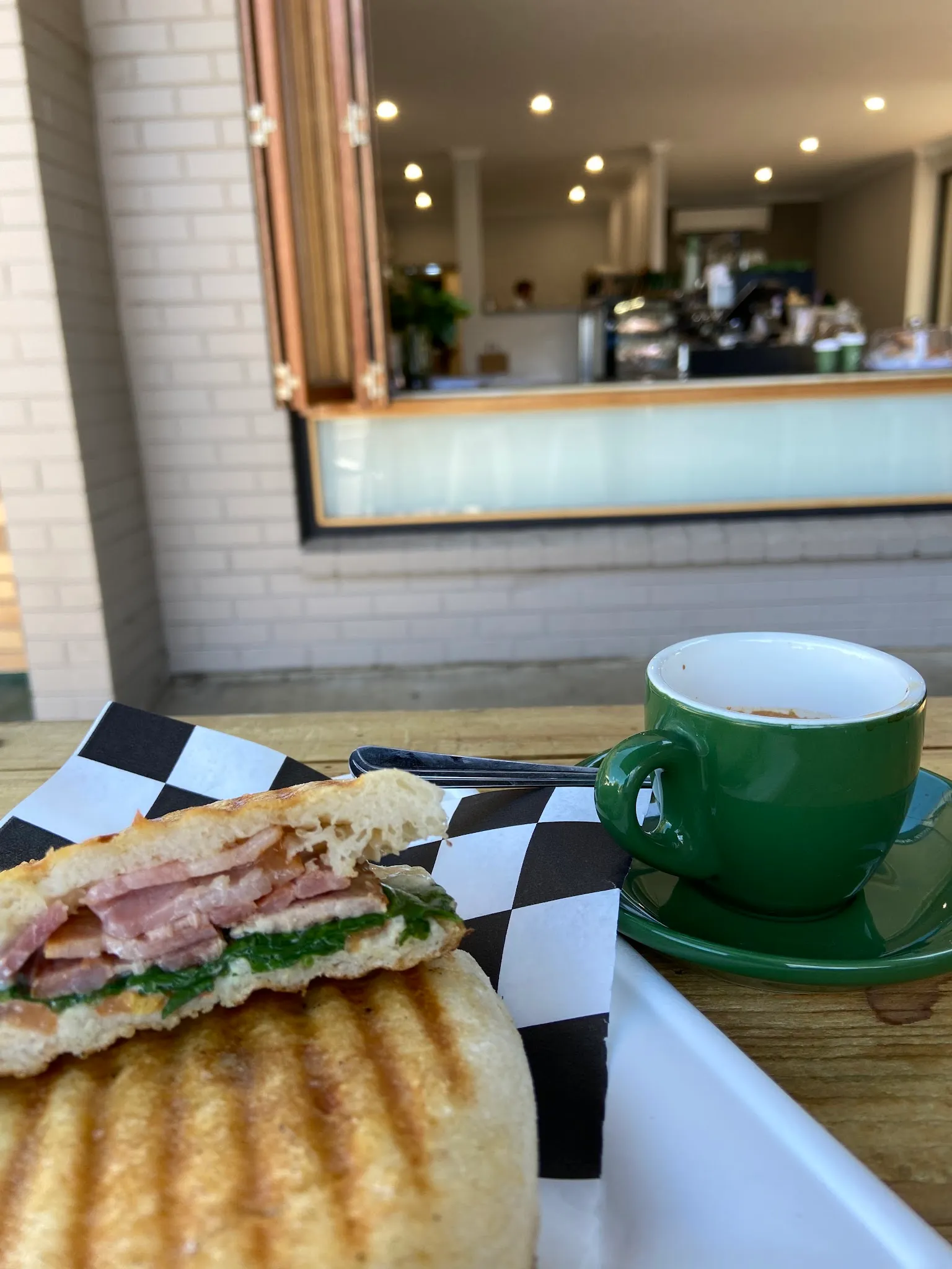 Grilled ham panini with green espresso cup on outdoor table, Cafe Biscotti interior visible behind