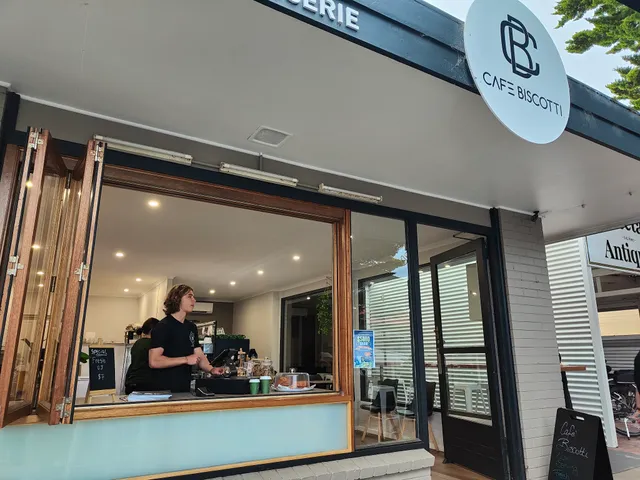 Barista working at Cafe Biscotti open service window with CB logo prominently above, Cowes